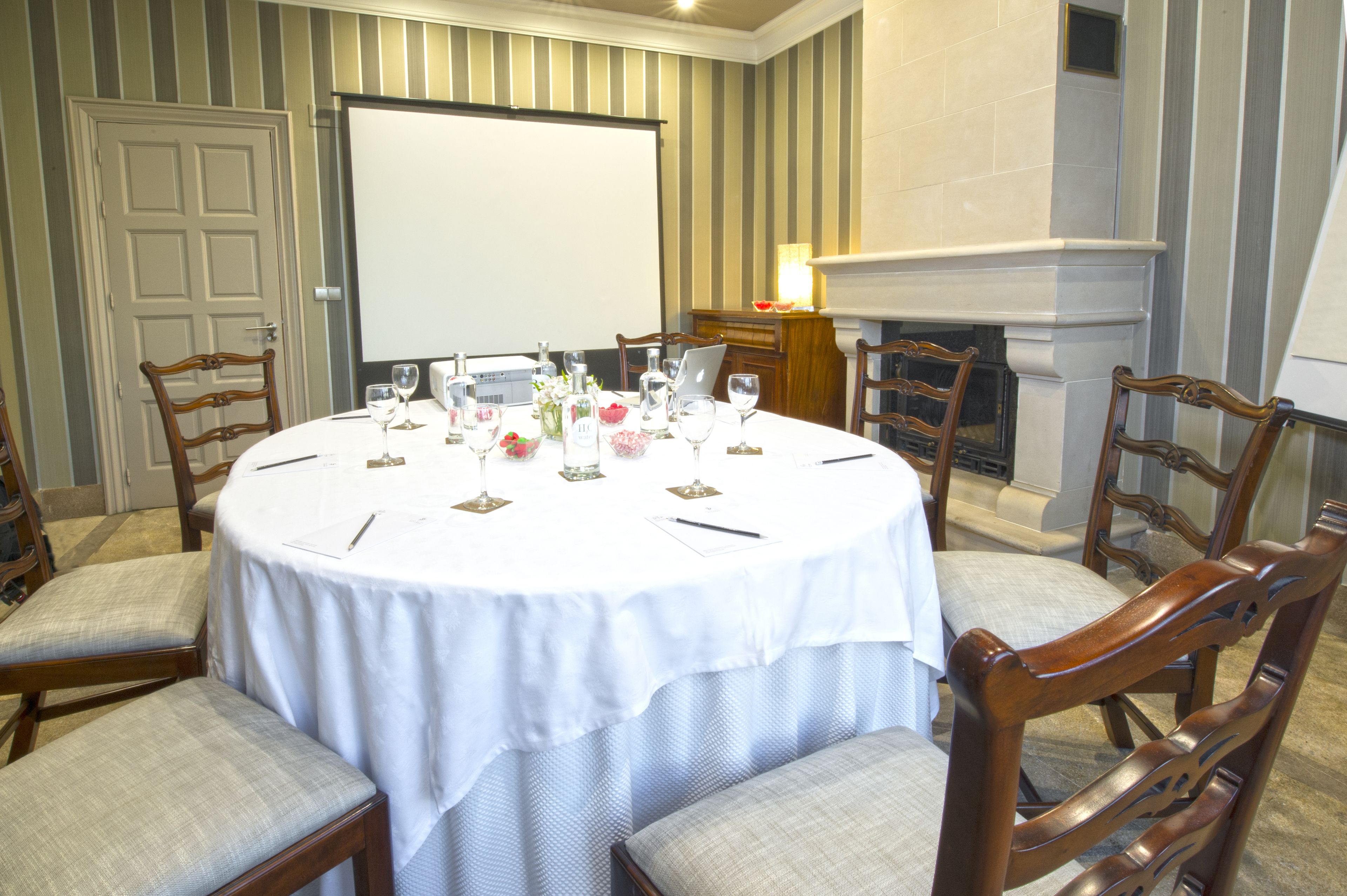 A conference room with a round table, chairs, a projector screen, and a fireplace.
