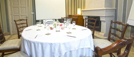 A conference room with a round table, chairs, a projector screen, and a fireplace.