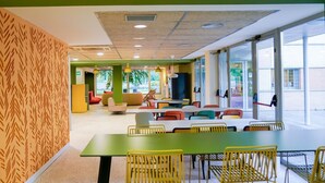 A modern dining area with green tables and yellow chairs, large windows, and a patterned wall. - Albergue Residencia Universitaria Resa Los Abedules - Campus Accomodation (Pamplona)