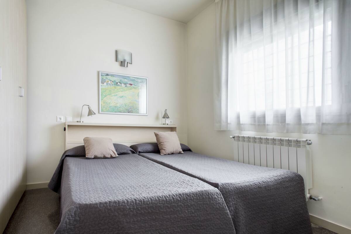 A bedroom with two beds, a painting on the wall, and a window with sheer curtains.