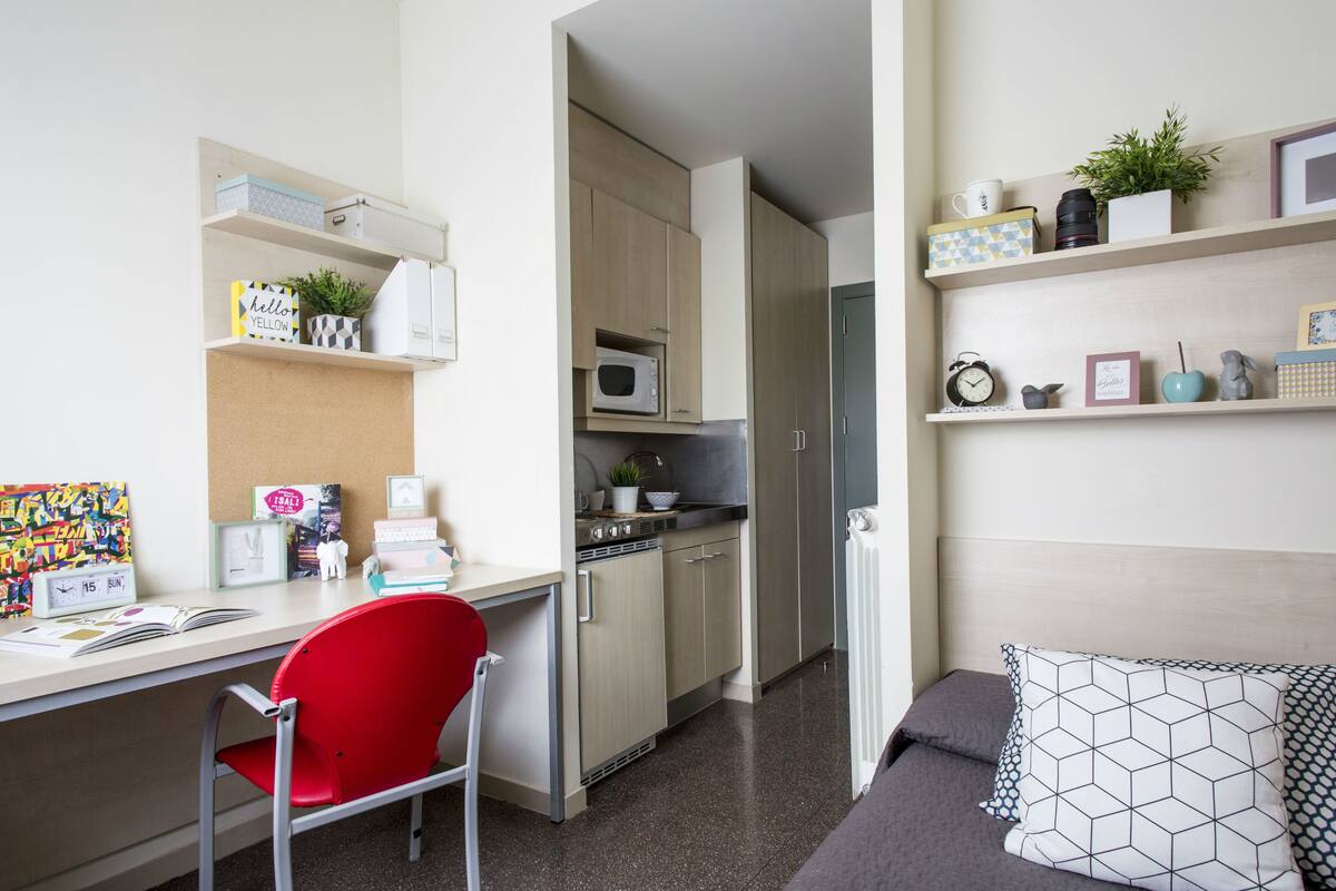 A compact living space with a kitchenette, a dining area, and a seating area with a red chair and a sofa.