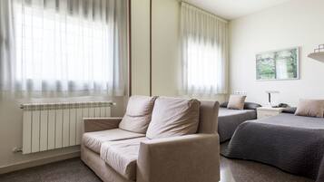 Habitación con sofá, dos camas, un radiador y un cuadro en la pared.