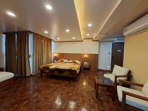 A hotel room with a large bed, wooden flooring, a sitting area with a table and chairs, and an air conditioning unit. - Hotel Utse (Kathmandu)