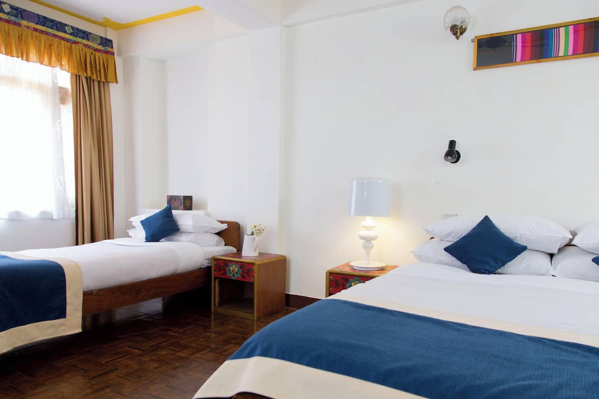 Habitación de hotel con dos camas, una mesita de noche con lámpara, luz empotrada en la pared y cortina colorida.