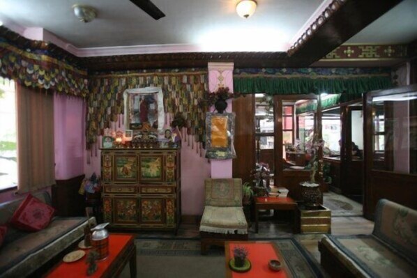 Quarto tradicional com sofá, um armário de madeira e uma cadeira. Há uma janela com cortinas e uma porta que dá para outro cômodo.