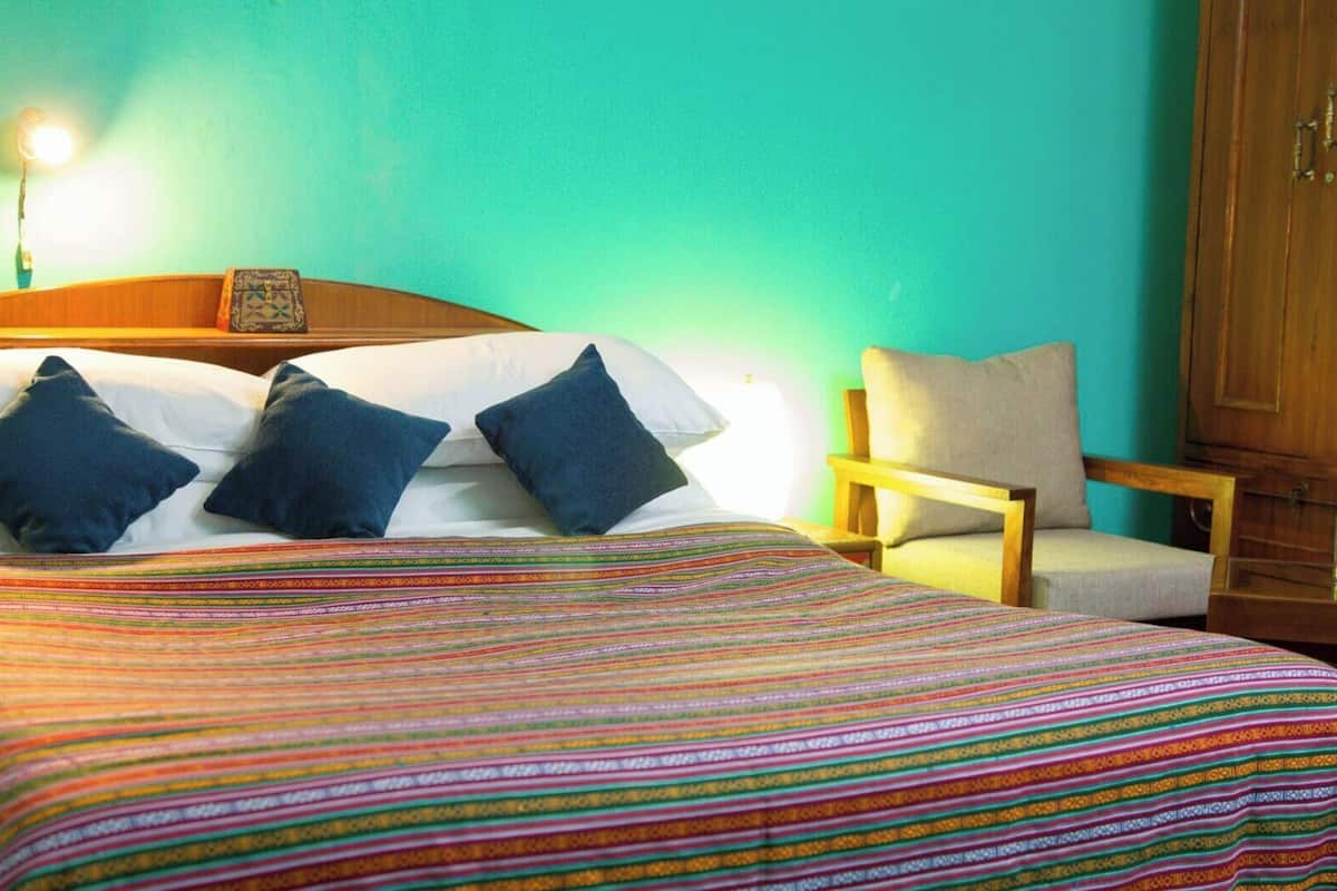 Una cama con un edredón a rayas de colores, dos almohadas, un cabecero de madera y una silla con cojín.