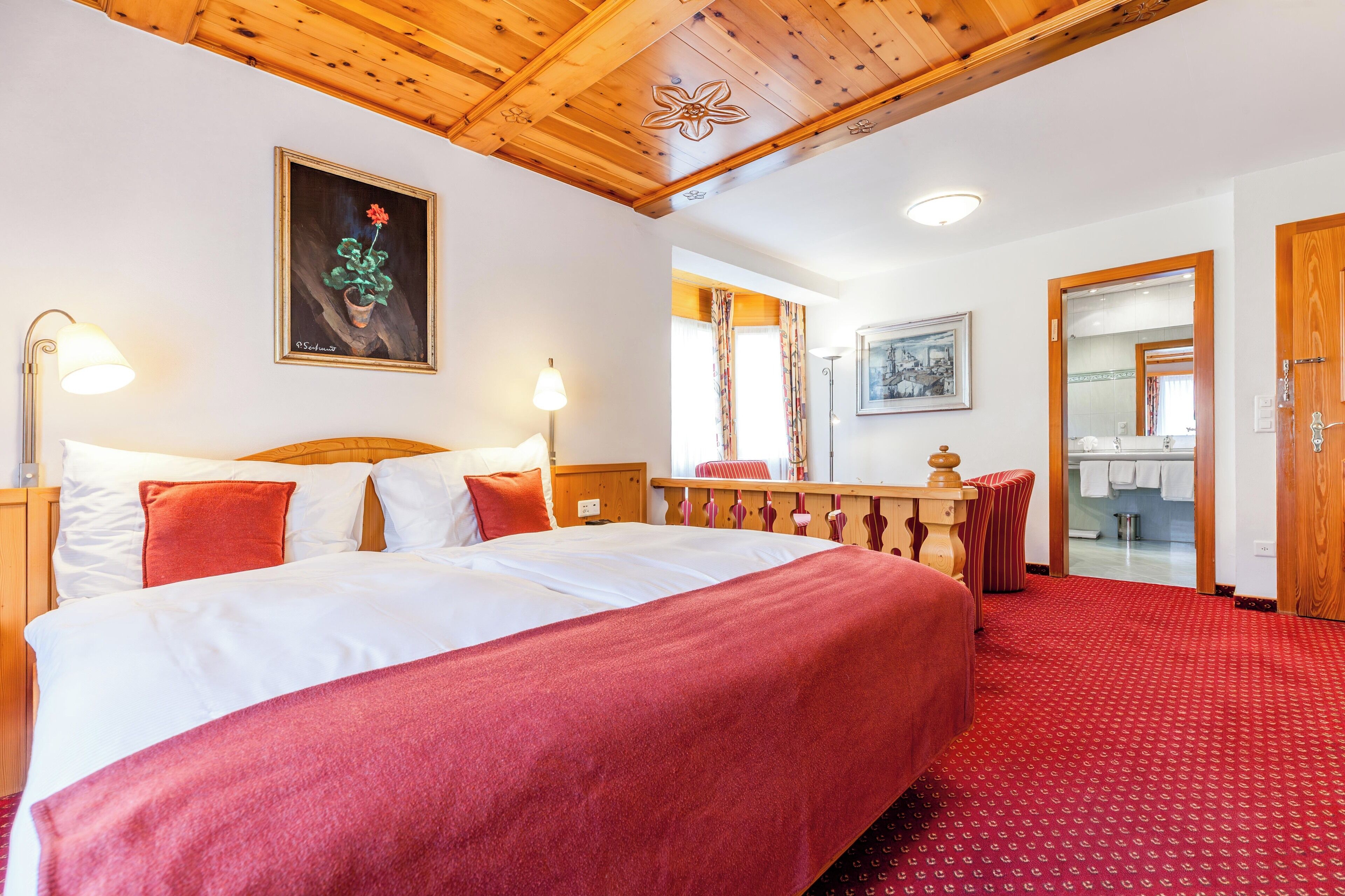 Ein Hotelzimmer mit einem großen Bett, Holzboden, einem Bild an der Wand und Blick ins Badezimmer.