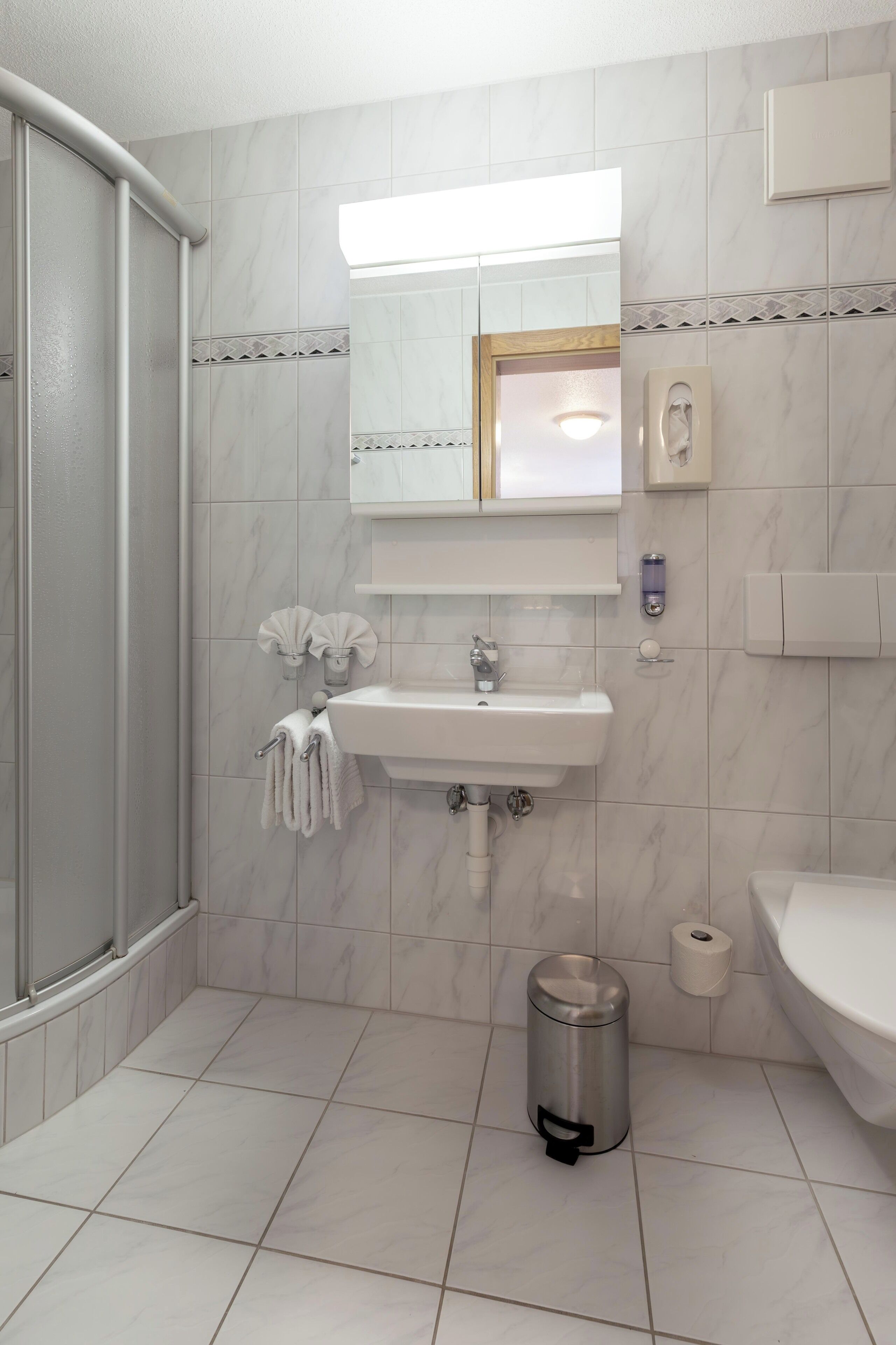 A bathroom with a shower, sink, toilet, and a trash can.