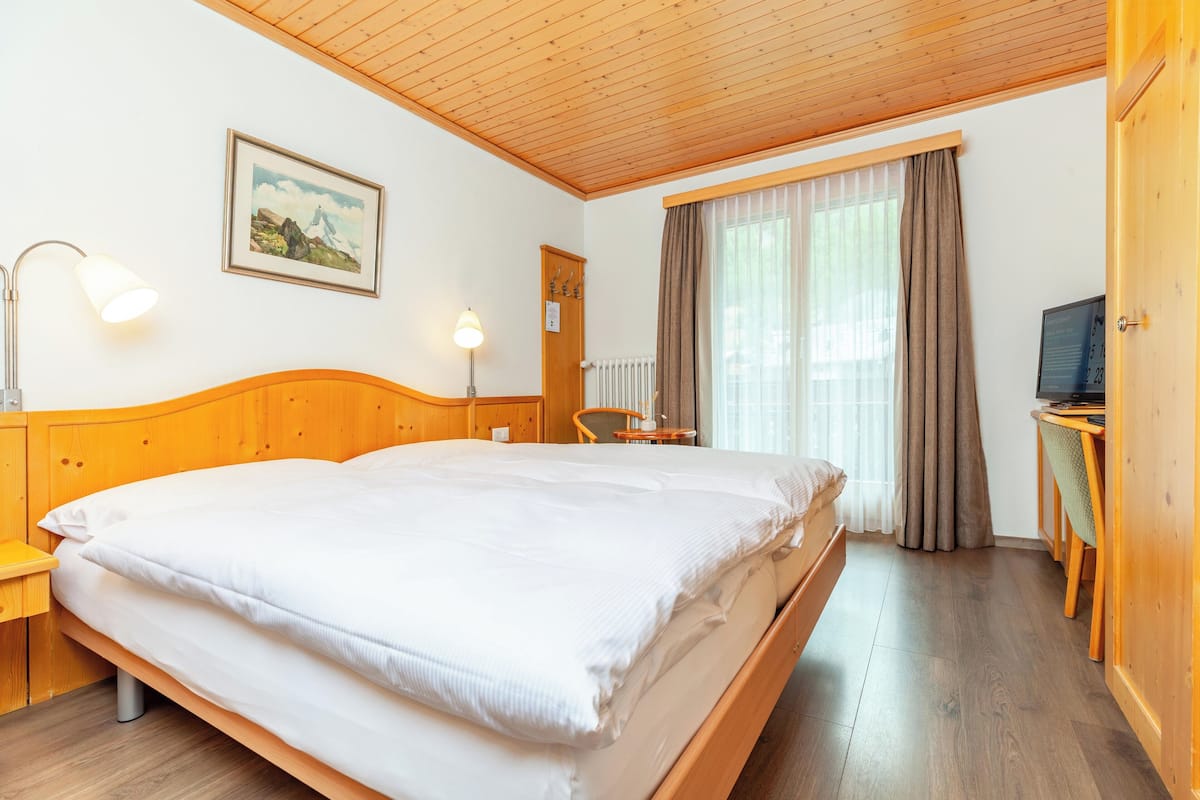 Habitación de hotel con cama de madera, escritorio, silla, televisor y ventana con cortinas.