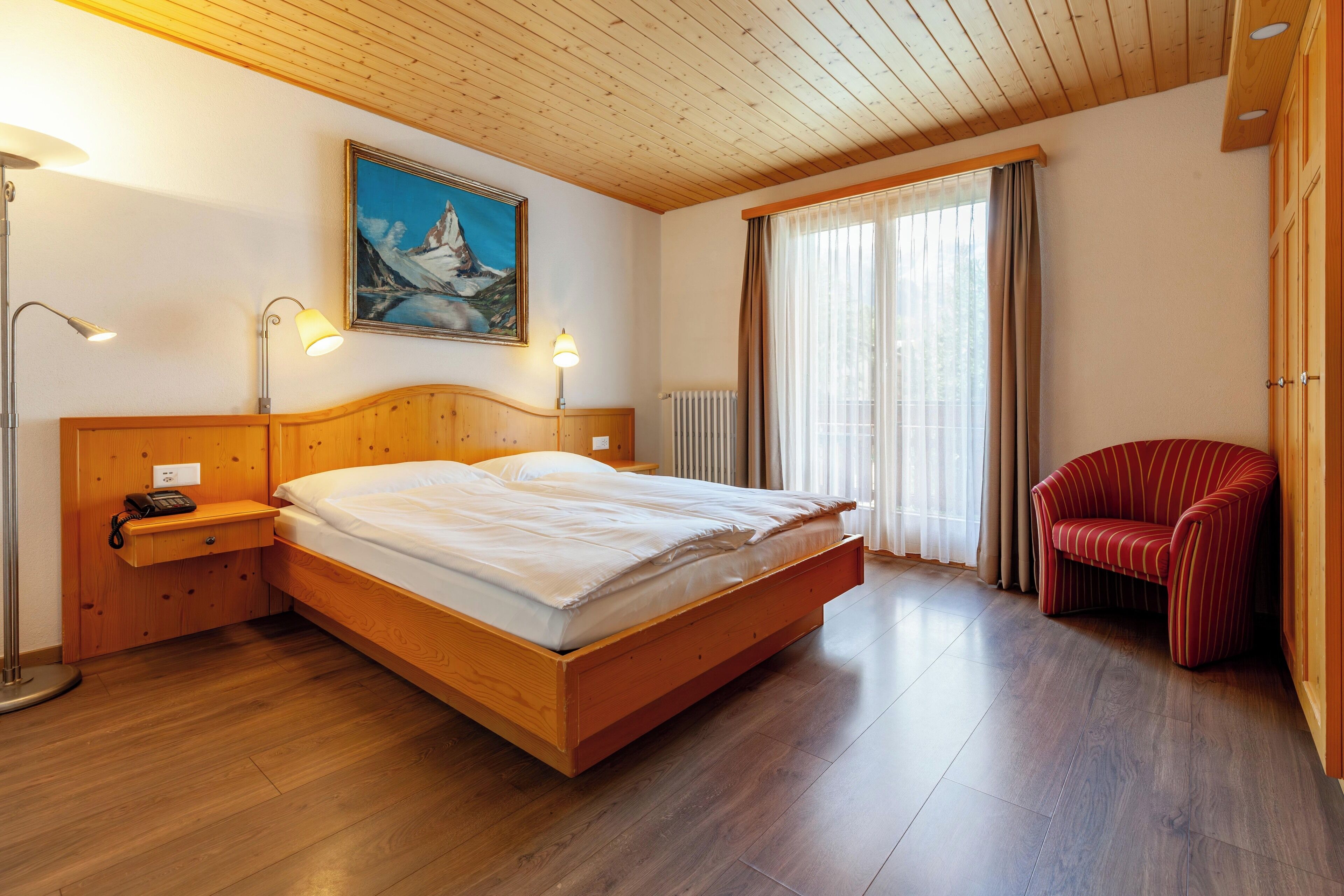 Una camera da letto con un letto di legno, lampade sui comodini, una sedia rossa e un quadro appeso al muro.