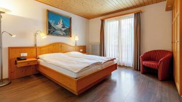 Una camera da letto con un letto di legno, lampade sui comodini, una sedia rossa e un quadro appeso al muro.