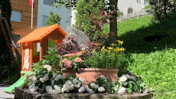Enjoy a serene outdoor space surrounded by lush plants and flowers, a wooden play structure, and a natural rock formation.