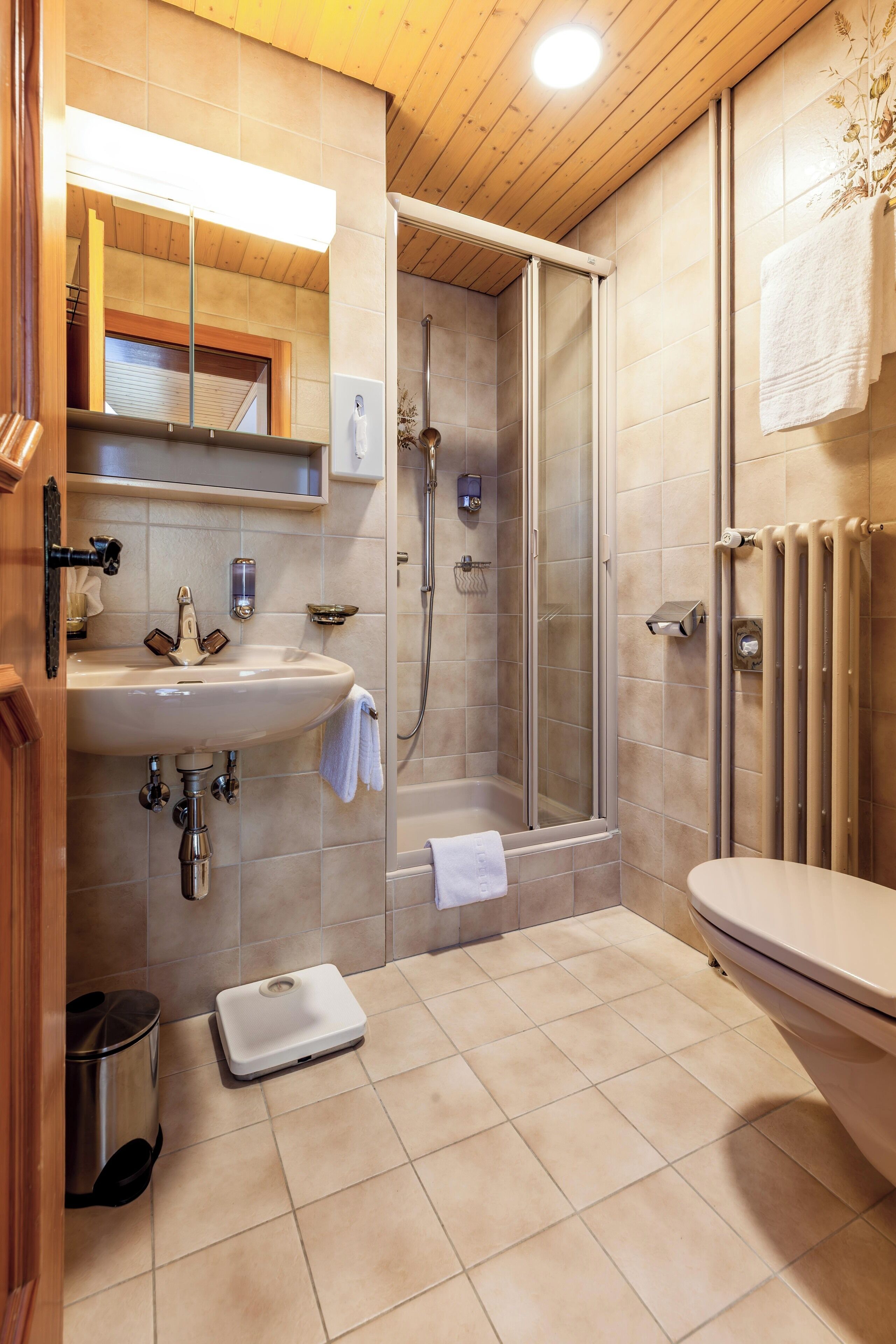 A bathroom with a sink, toilet, shower, and a scale on the floor.