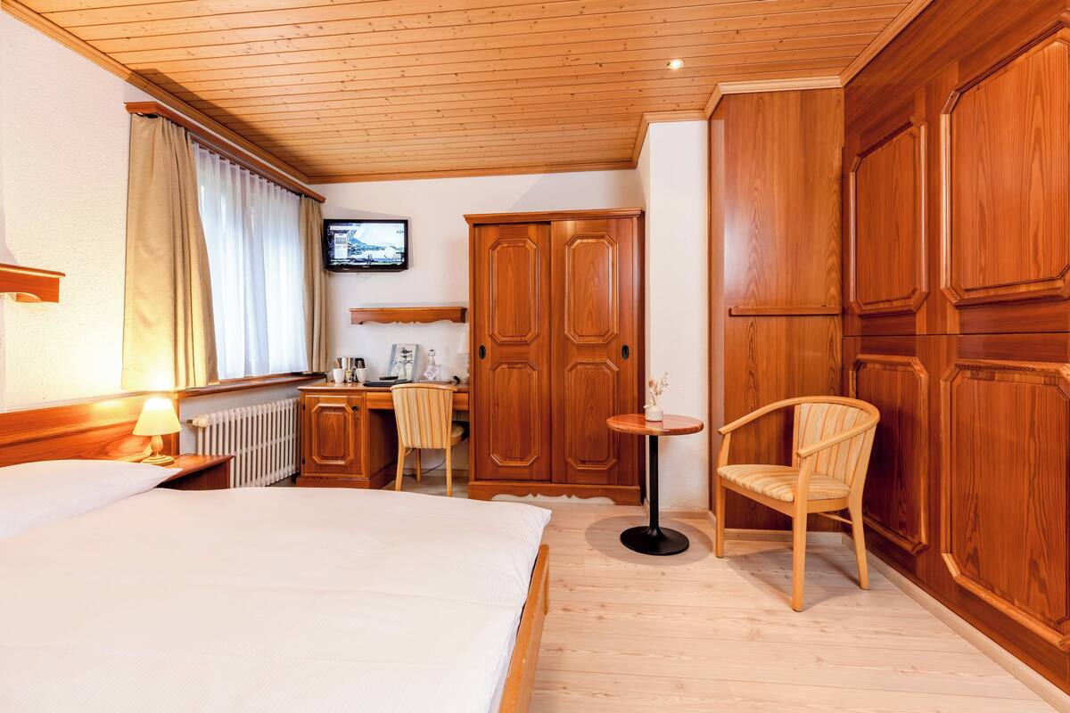 Habitación de hotel con cama, armario de madera, escritorio, silla y una mesita redonda.