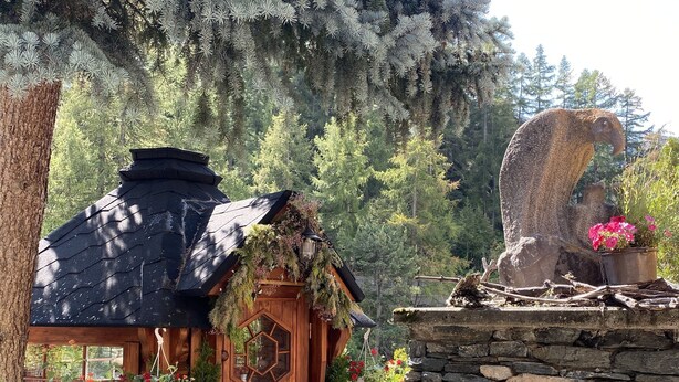 A wooden cabin with a thatched roof, surrounded by lush greenery and a stone wall. - Alpenblick (Zermatt)