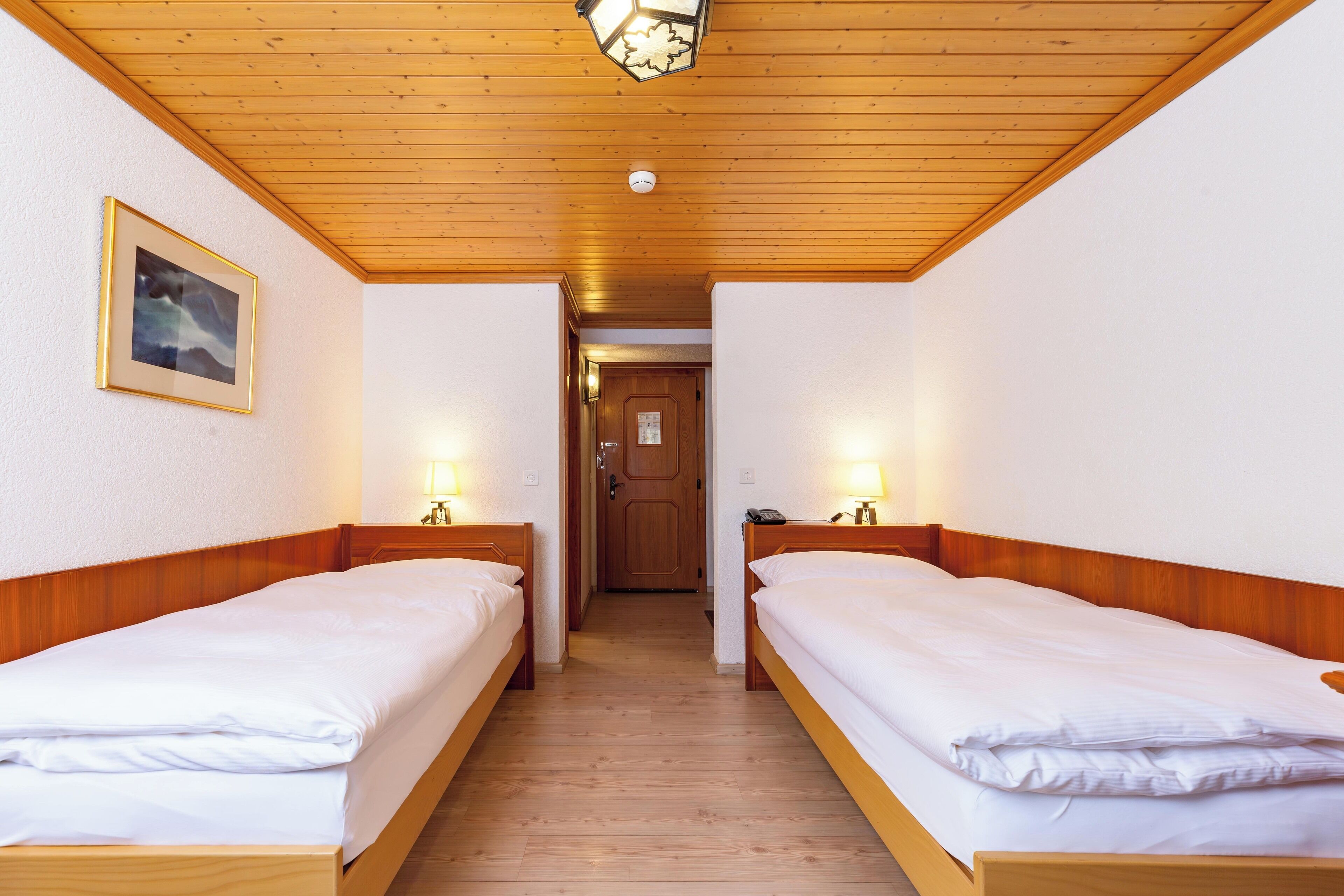 Una habitación de hotel con dos camas individuales, cabeceros de madera, un cuadro enmarcado en la pared y techo de madera.