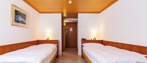 Una habitación de hotel con dos camas individuales, cabeceros de madera, un cuadro enmarcado en la pared y techo de madera.