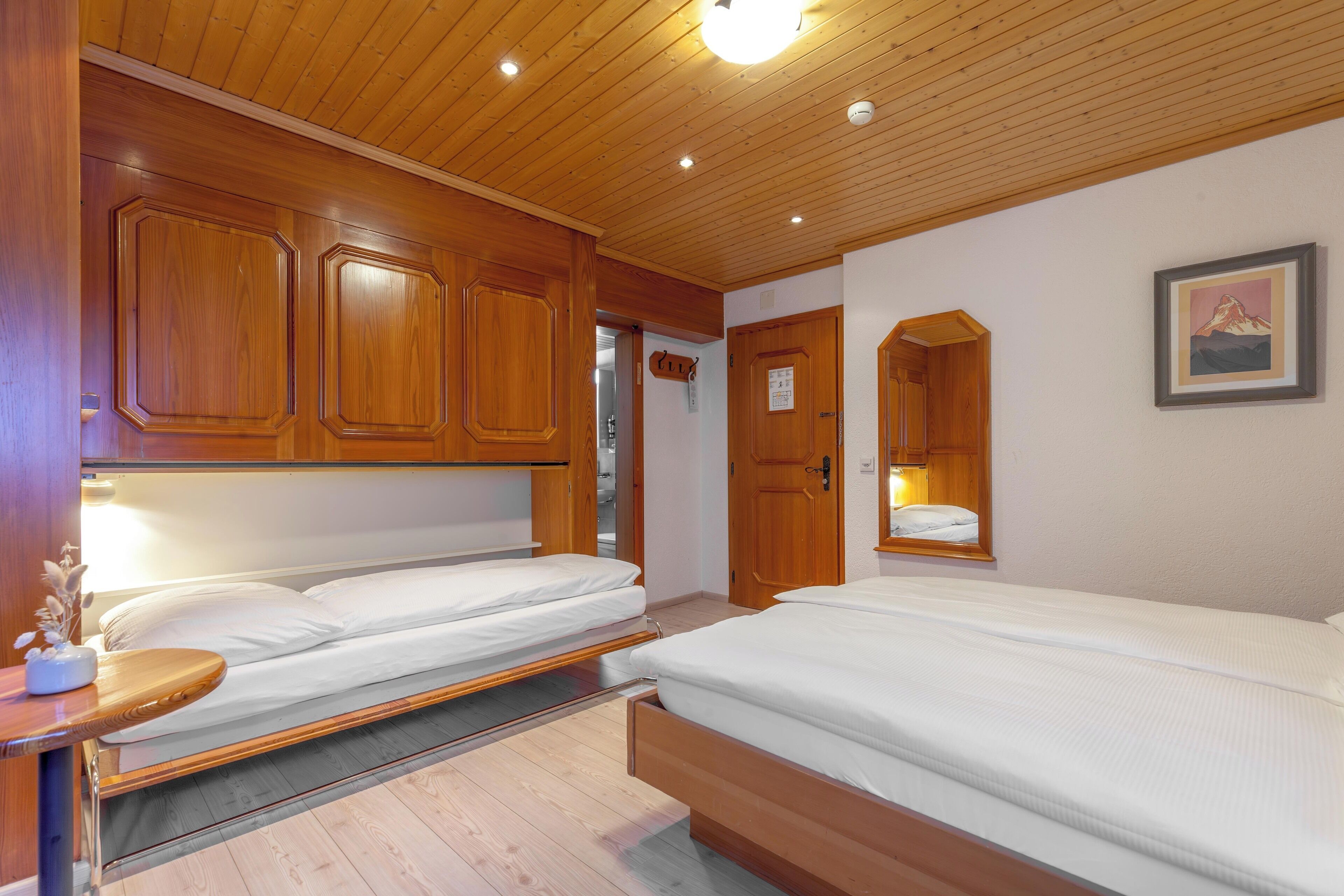 Une chambre avec deux lits, des armoires en bois et un tableau encadré au mur.