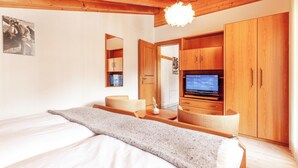 A modern bedroom with a large bed, wooden wardrobe, and a television displaying a weather forecast. - Alpenblick (Zermatt)
