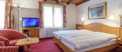 Habitación de hotel con una cama, televisión, escritorio, silla y ventana con cortinas.