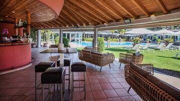 An outdoor patio area with wicker furniture, a bar, and a pool view.