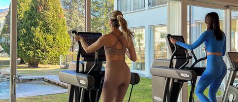 A gym with treadmills and a large window offering a view of a landscaped area.