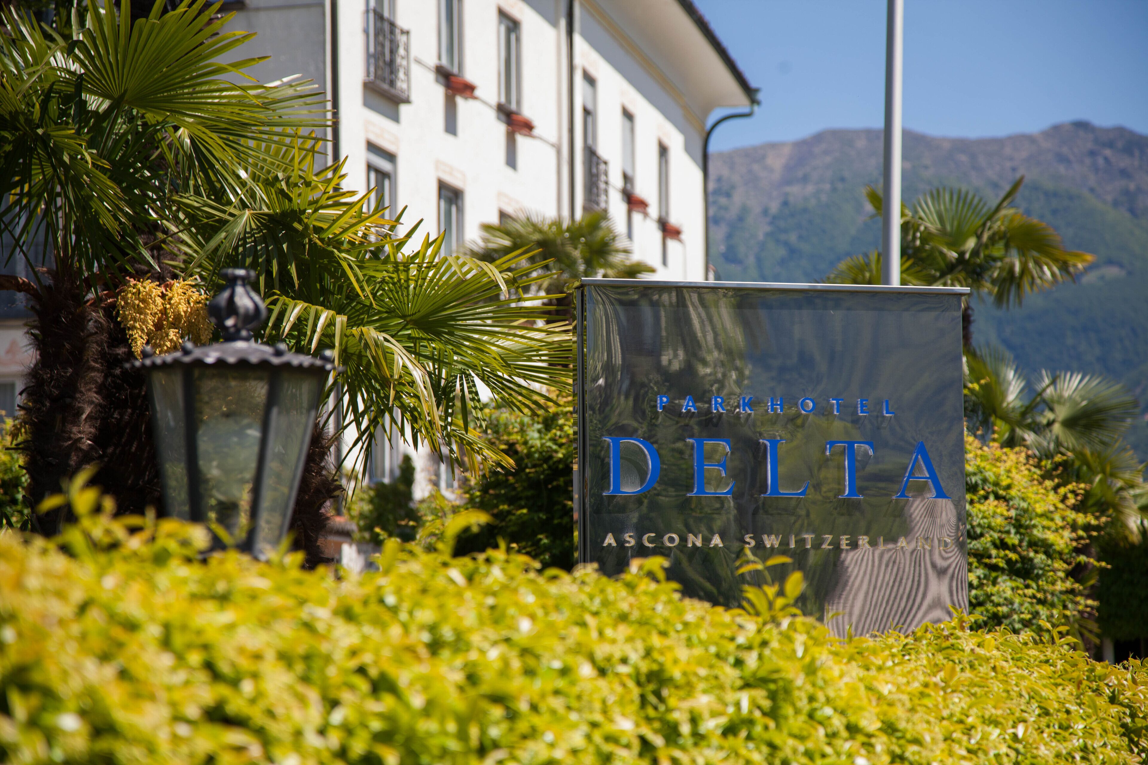 A sign for Park Hotel Delta with a view of a mountain in the background.