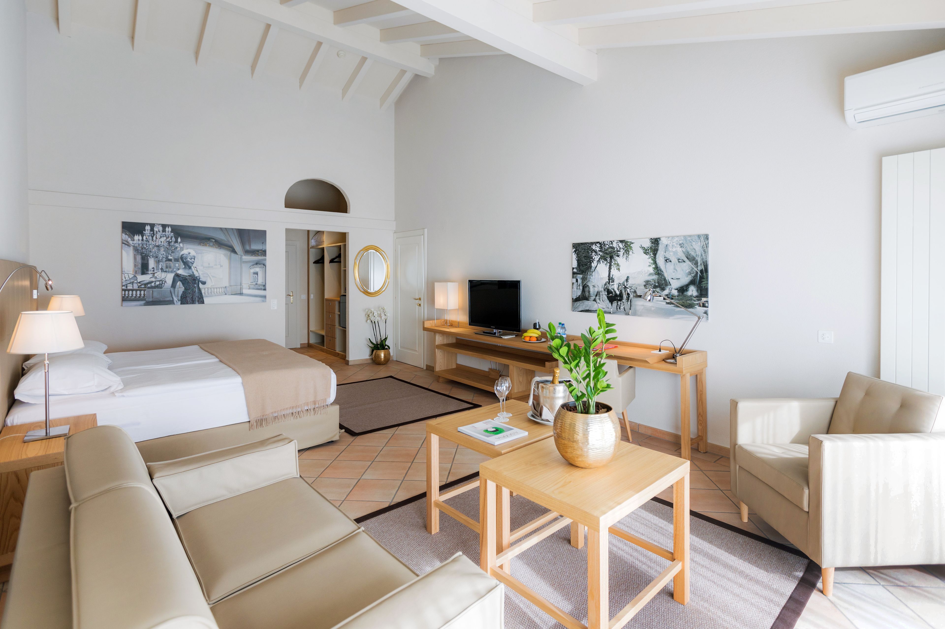 A modern hotel room with a bed, sofa, TV, and a dining area with a table and chairs.