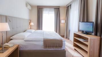 Habitación de hotel con cama, lámparas de noche, televisor sobre un soporte de madera y ventana con cortinas.