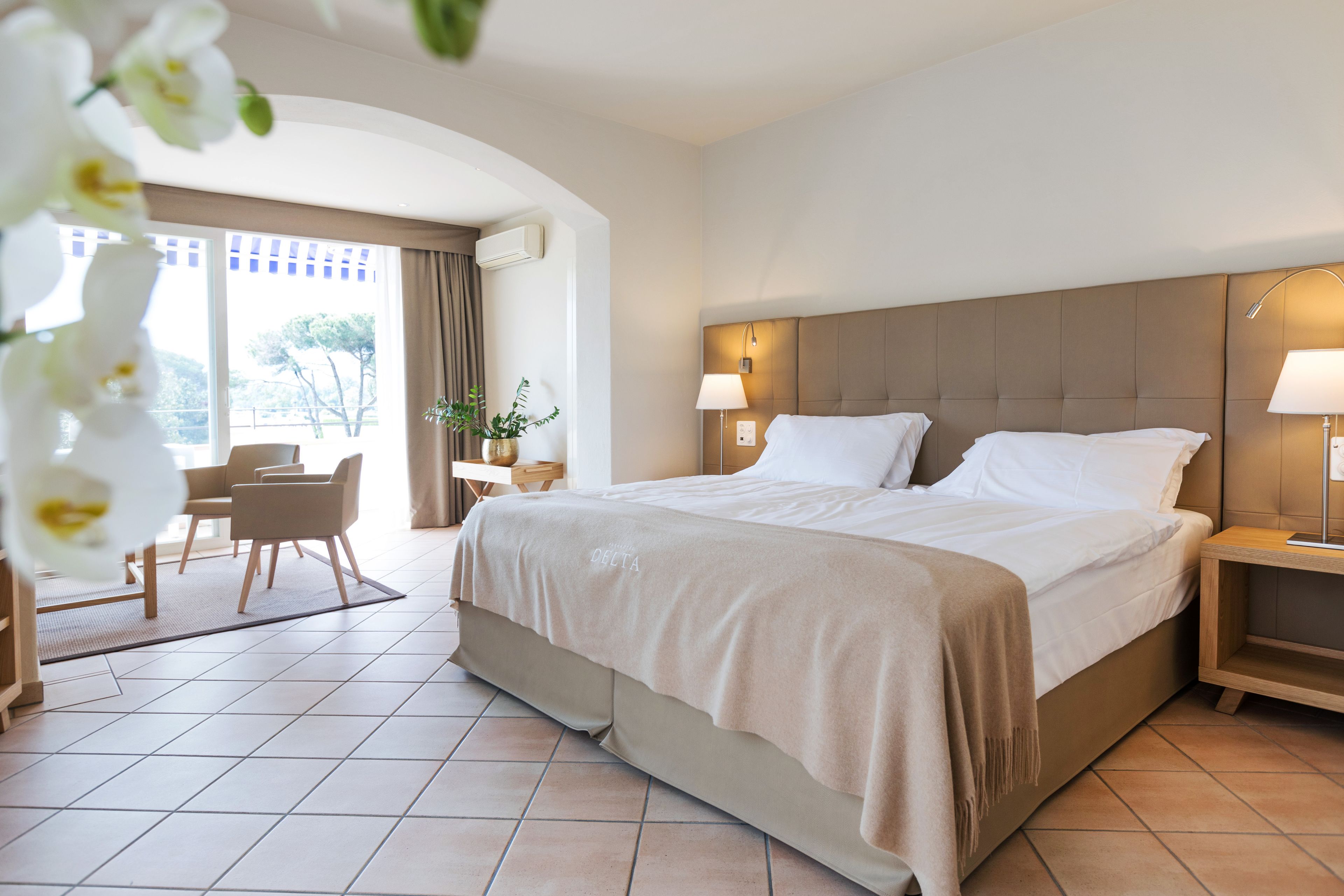 A hotel room with a large bed, a desk, a chair, and a view of the outdoors.