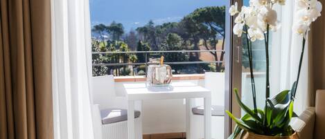 A balcony with a white table and chairs, a vase with white flowers, and a view of mountains and trees.