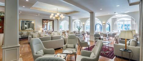 A spacious lobby with a high ceiling, elegant chandeliers, and a mix of seating areas including sofas and armchairs.