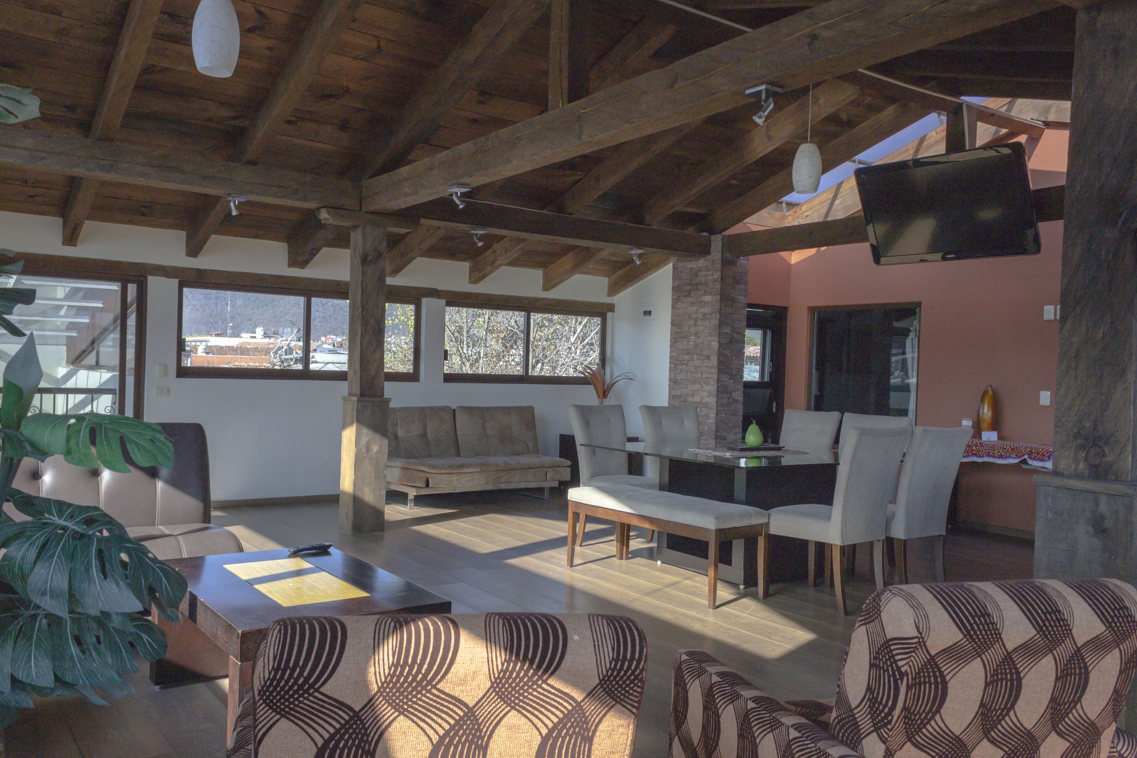 Amplia sala de estar con techo de madera, un sofá, una mesa de comedor con sillas y un televisor montado en la pared.