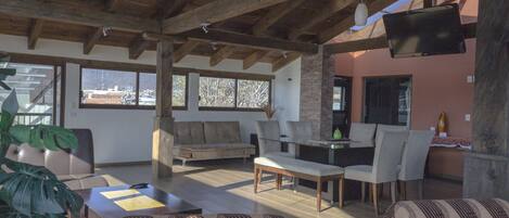 Amplia sala de estar con techo de madera, un sofá, una mesa de comedor con sillas y un televisor montado en la pared.