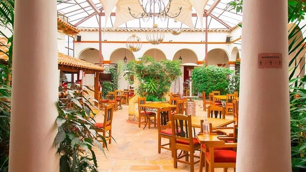 An indoor dining area with wooden tables and chairs, surrounded by columns and arches, under a glass ceiling. - Hotel Plaza Magnolias (San Cristóbal de las Casas)