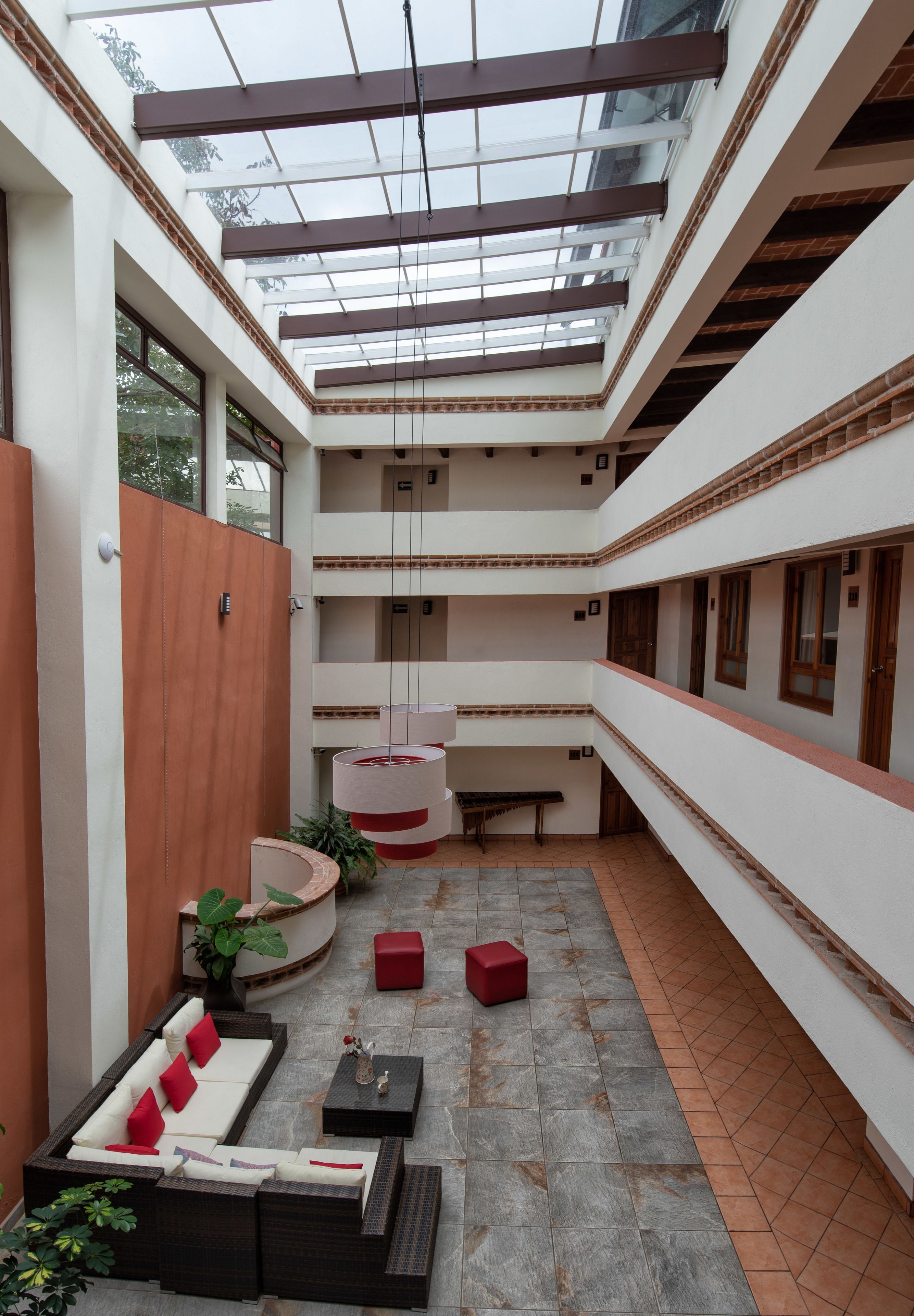 A multi-level atrium with a glass ceiling, a seating area with a sofa and red cushions, and a small table with a vase.
