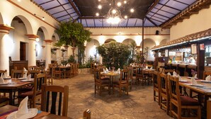 A restaurant with a high ceiling, arched columns, and wooden tables and chairs. - Hotel Plaza Magnolias (San Cristóbal de las Casas)
