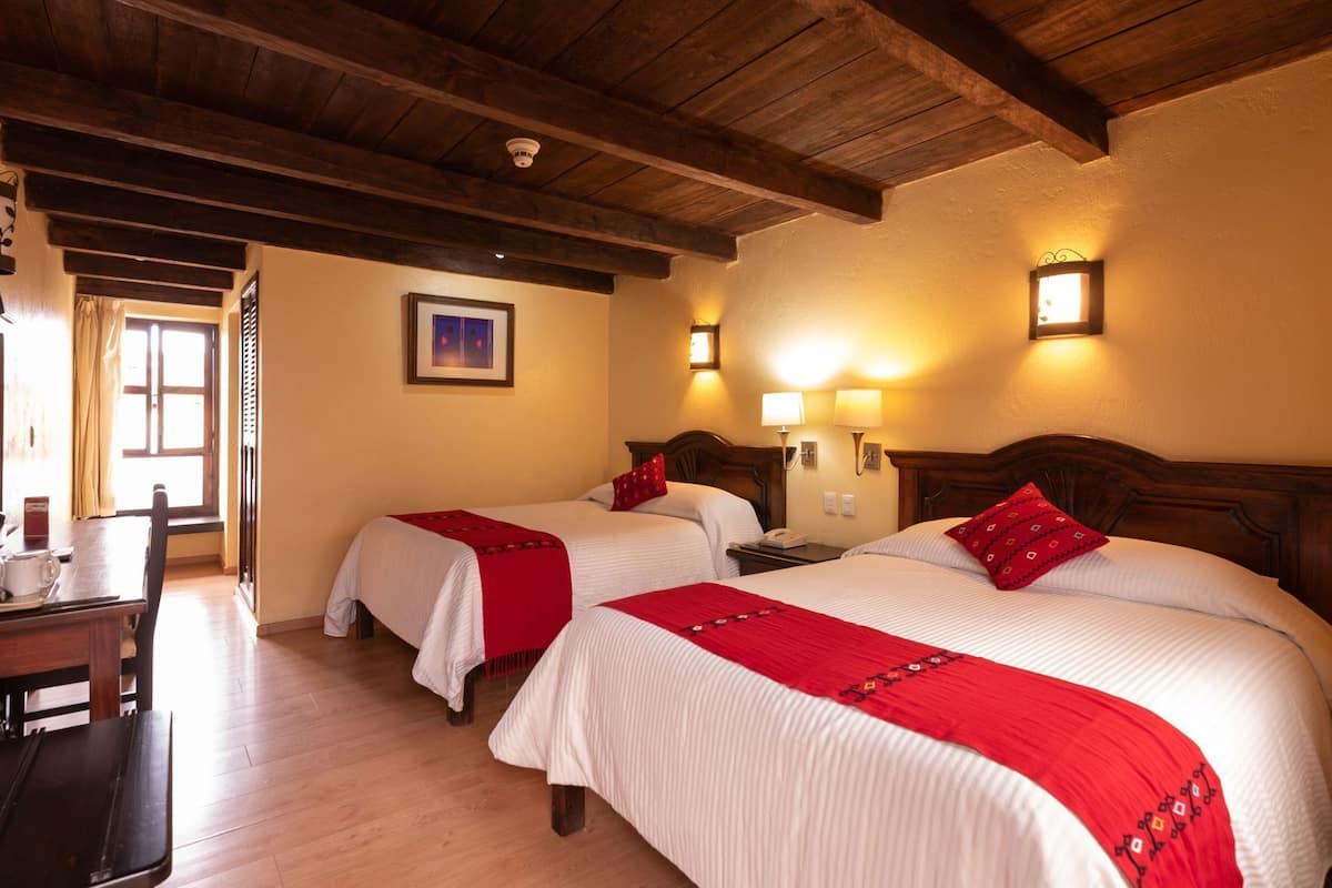 Une chambre d’hôtel avec deux lits, des poutres en bois au plafond, un bureau avec une chaise et une fenêtre avec des rideaux.
