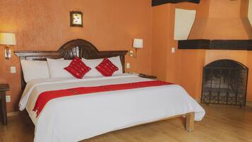 Habitación de hotel con una cama de madera, ropa de cama blanca, almohadas rojas, una chimenea y apliques de pared.