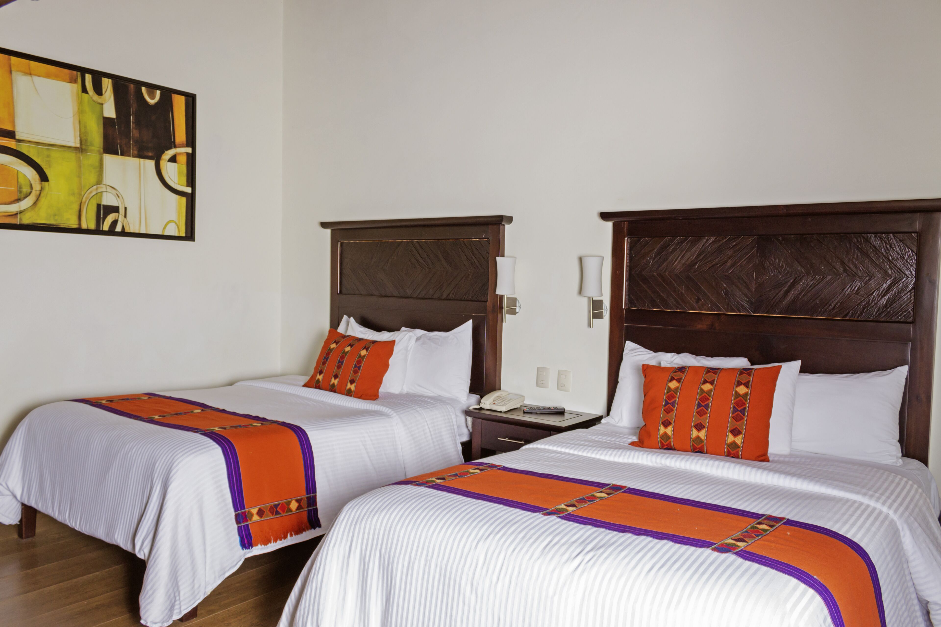Two double beds with wooden headboards, white bedding, and orange decorative pillows.