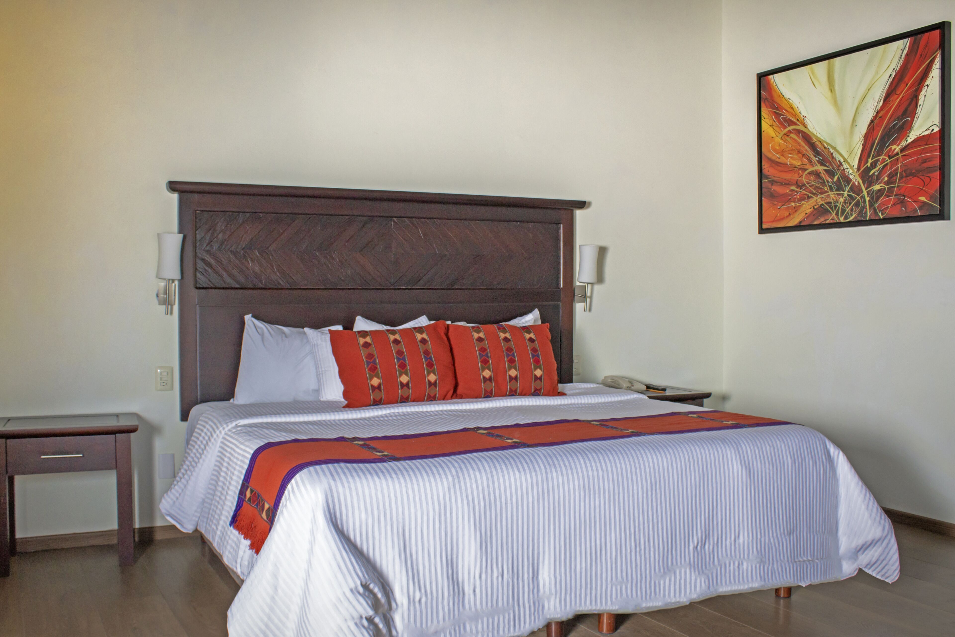A hotel room with a large bed, a nightstand, a lamp, and a painting on the wall.