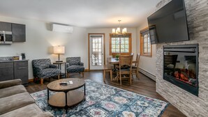 A modern living room with a fireplace, a flat-screen TV, a dining area with a table and chairs, and a kitchen area with a microwave and cabinets. - Grey Fox Inn (Stowe)