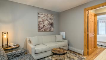 A modern living room with a light grey sofa, a patterned armchair, a small round table, and a large abstract painting on the wall.