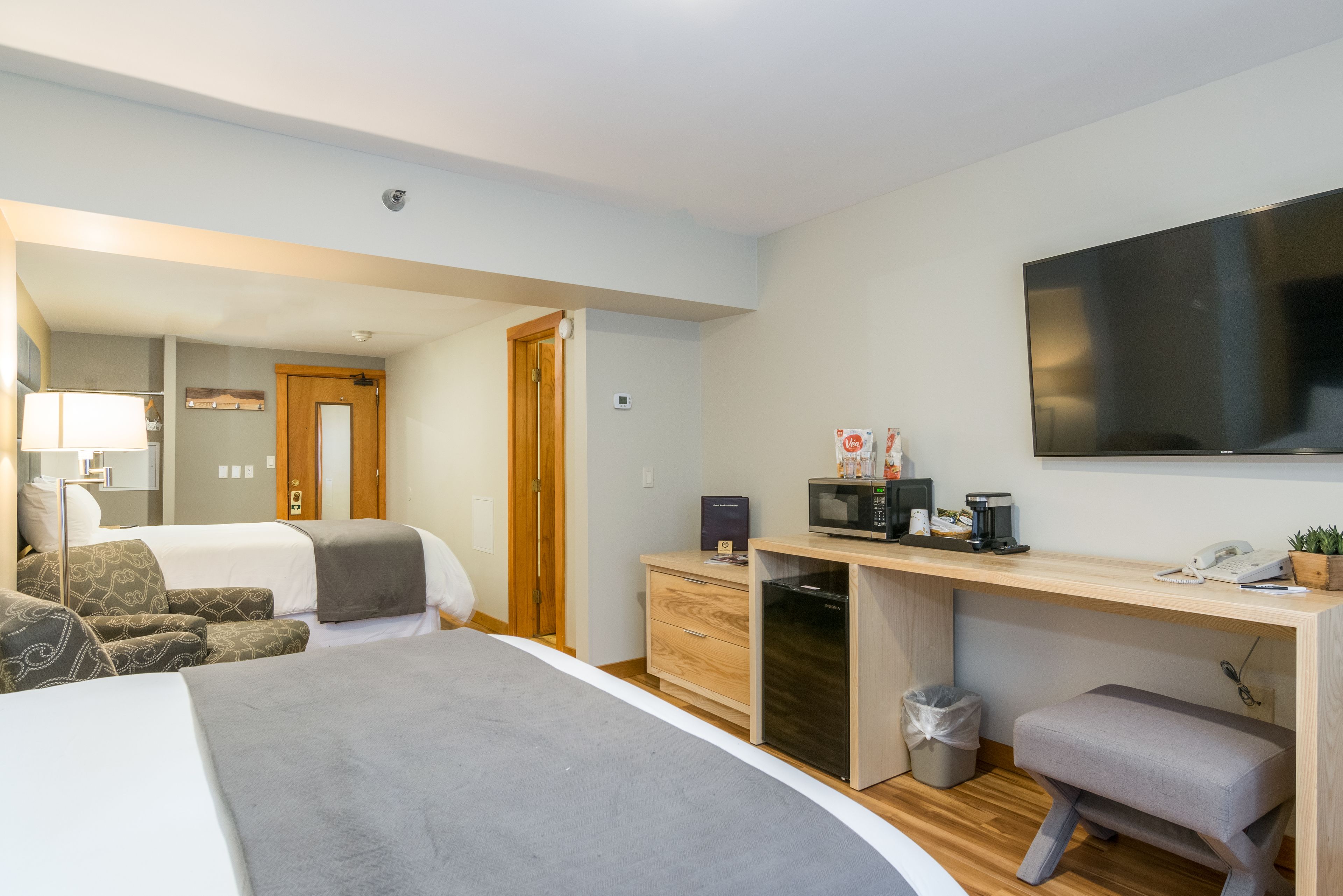 Ett modernt hotellrum med en säng, ett skrivbord med en dator, en mikrovågsugn och en liten papperskorg.