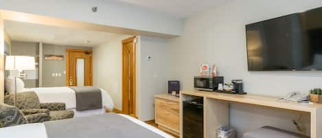 Une chambre d’hôtel moderne équipée d’un lit, d’un bureau avec un ordinateur, d’un four à micro-ondes et d’une petite poubelle.