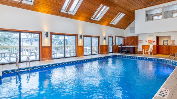 A large indoor swimming pool with wooden beams and skylights, surrounded by large windows and a deck area. - Grey Fox Inn (Stowe)