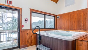 A wooden-finished bathroom with a hot tub, a window with a view of snow-covered trees, and an exit sign. - Grey Fox Inn (Stowe)