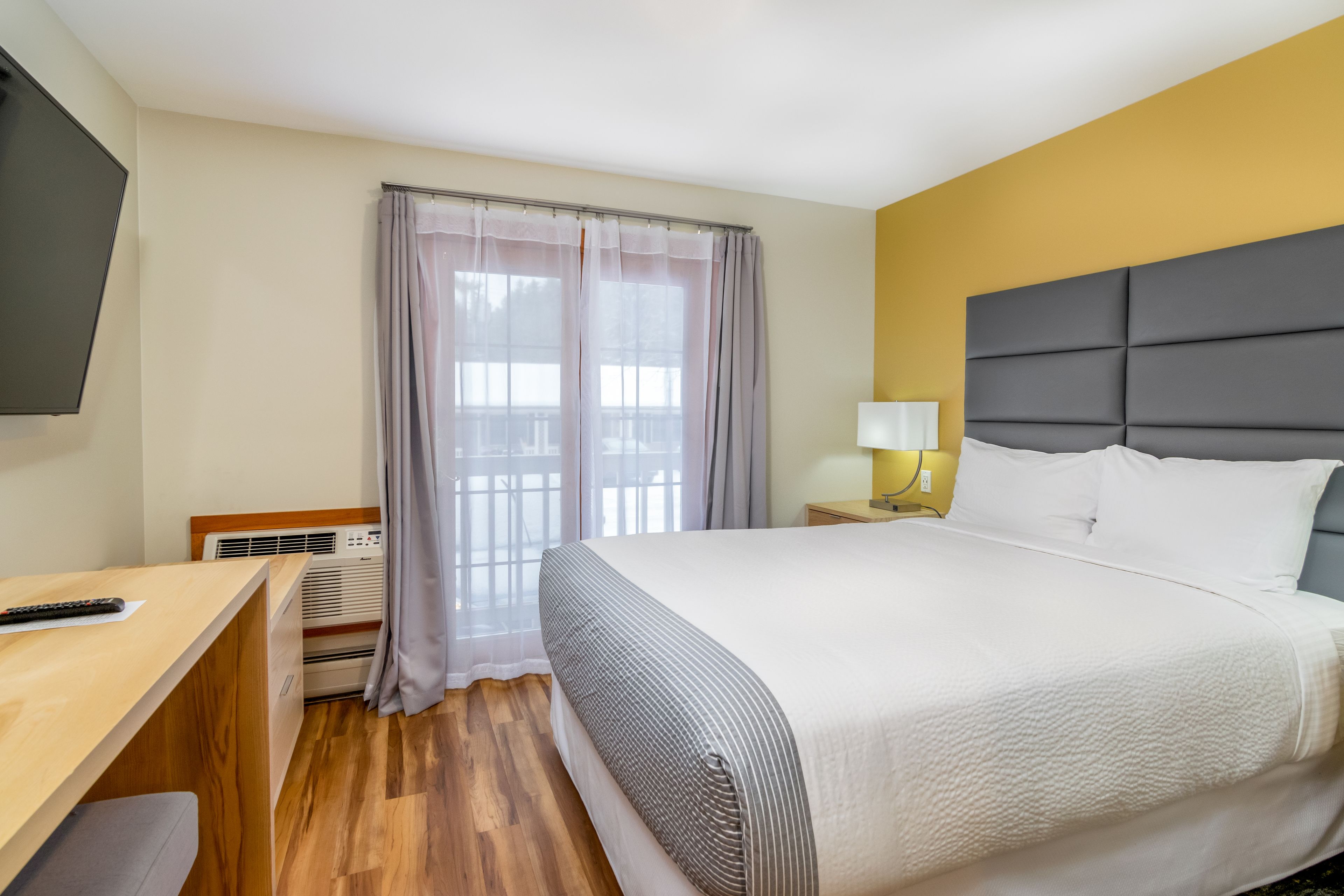A hotel room with a bed, a desk, a chair, a lamp, and a window with curtains.