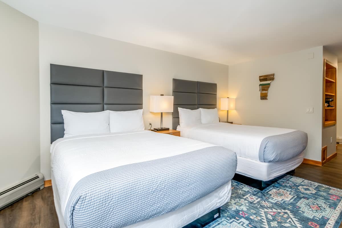 A hotel room with two beds, a small desk, and a nightstand with lamps.