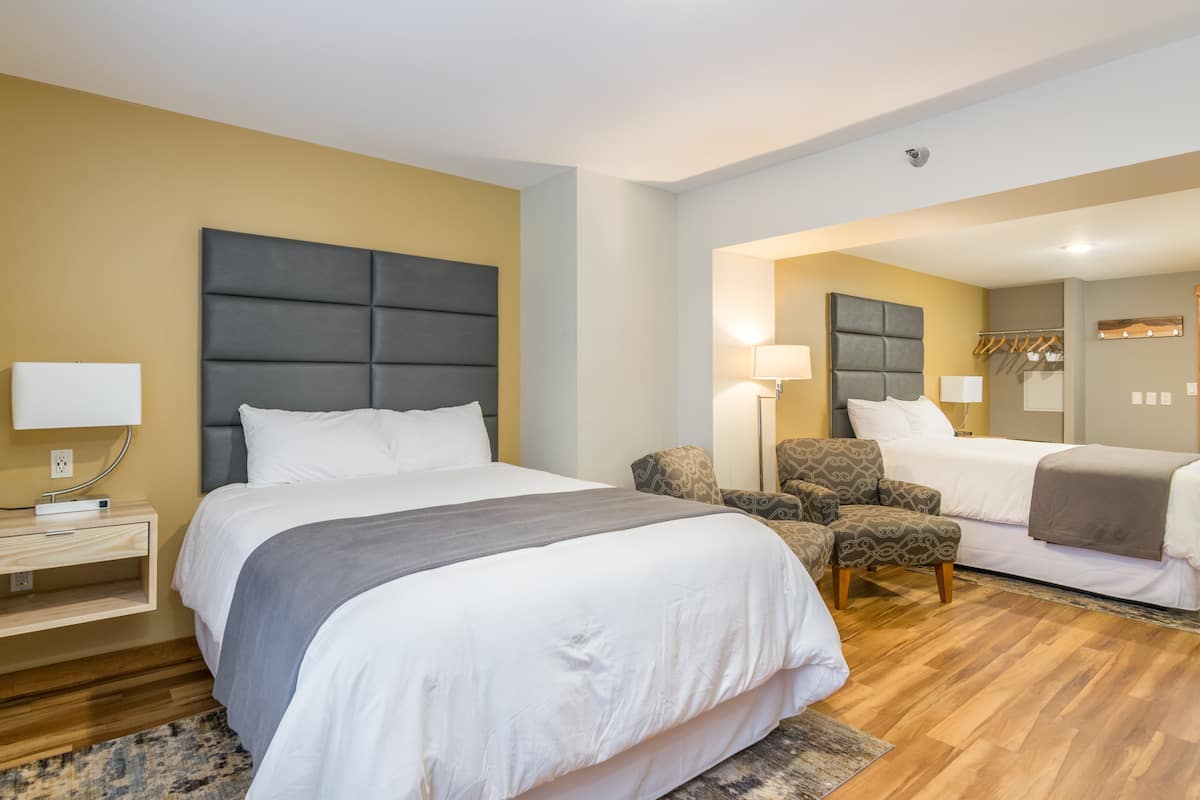 A hotel room with a large bed, a smaller bed, a seating area with patterned chairs, and a bedside table with a lamp.